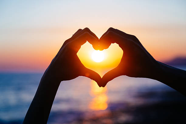 hands forming a heart shape with sunset silhouette. Copy space text.