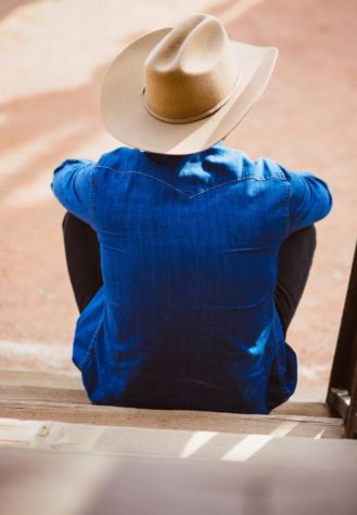 A cowboy sitting on steps with his back to the camera