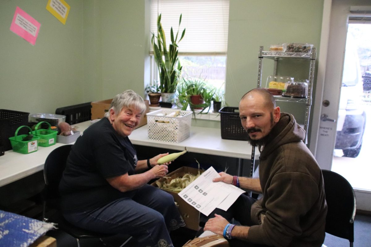 Susan Campbell, volunteer at Brunswick Family Assistance, Leland Office, shucks corn for the mobile food pantry.  Christopher Rivenbark says, "good job!"